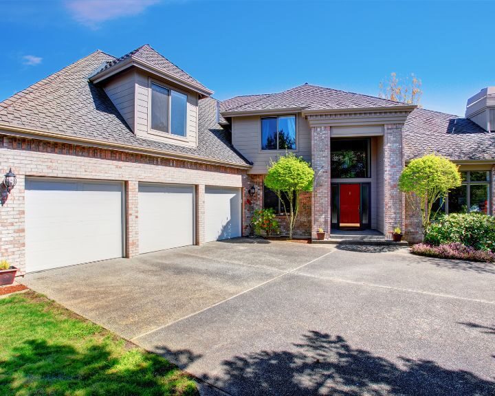 A large house with a concrete driveway and red door in the city.