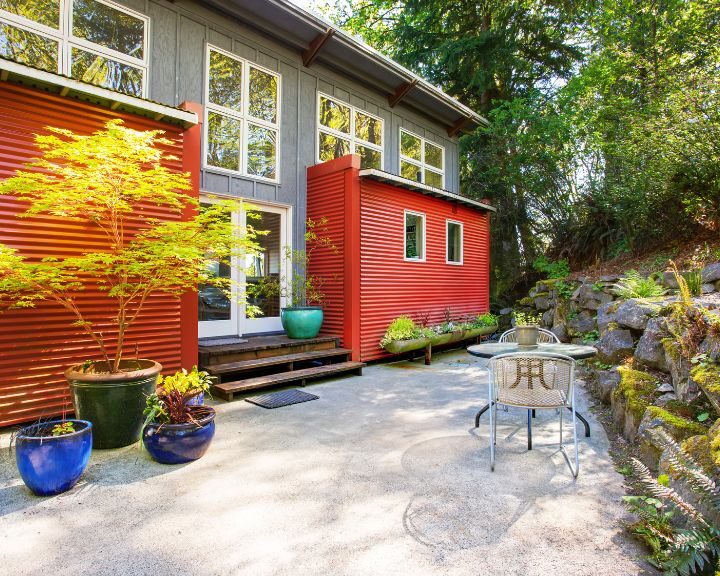 A city house concrete patio with a red siding and a green tree.