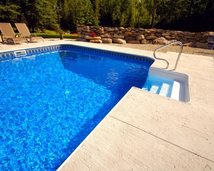a concrete pool decks surrounded by lawn chairs.