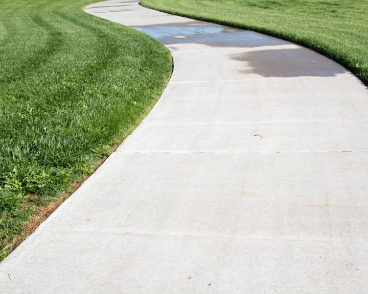 A concrete sidewalk bordered by a grassy field in the city.