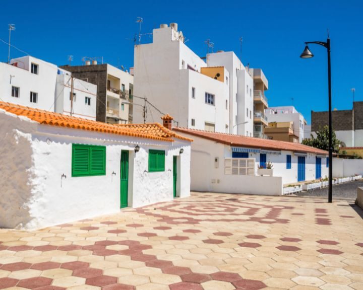 A white building with green shutters and a red roof in the city.